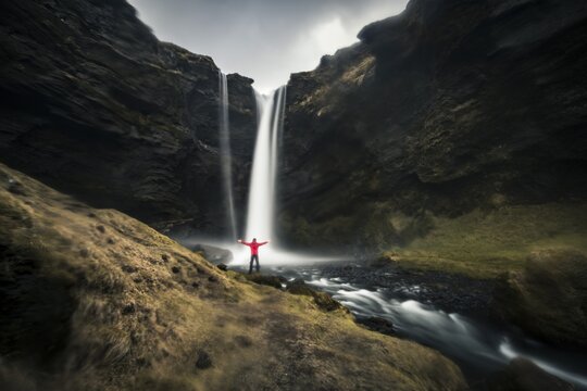 Man in red jacket in front of Kvernufoss waterfall in a gorge, dramatic atmosphere, time exposure, near Sk&oacute;gafoss, Southurland, Iceland