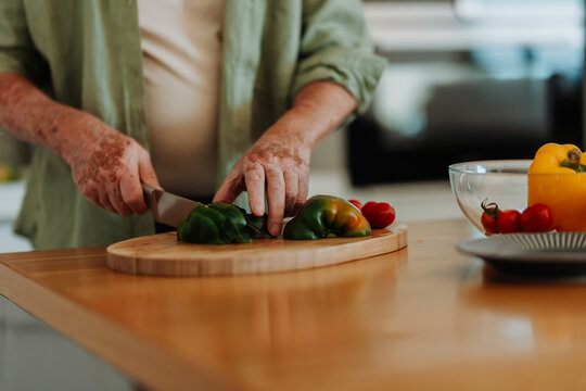 Close-up of senior man preparing vegetable, cutting at wooden board.