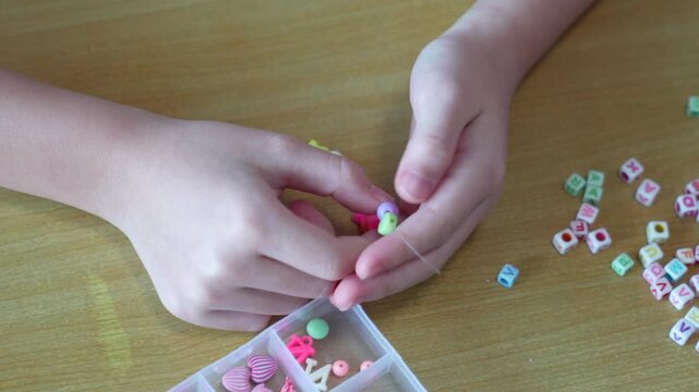 The bead activity supports careful finger movement, tactile practice, and cooperative learning while children create handmade jewelry from divided compartments.