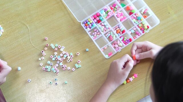 The bead activity supports careful finger movement, tactile practice, and cooperative learning while children create handmade jewelry from divided compartments.