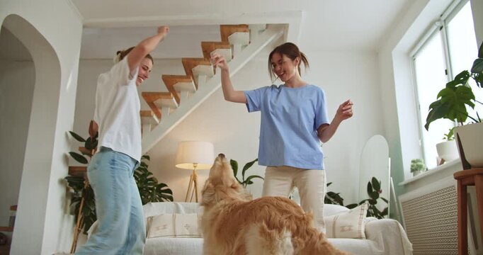 Happy lesbian couple dancing with their golden retriever at home