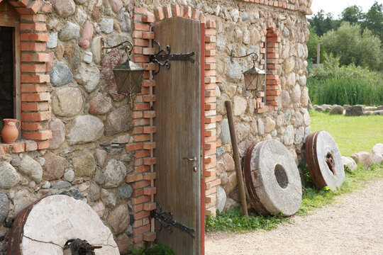 Stone building with wooden door and millstones near grassy area in rural setting during daytime