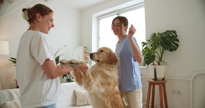 Two happy women dancing and playing with their golden retriever dog at home