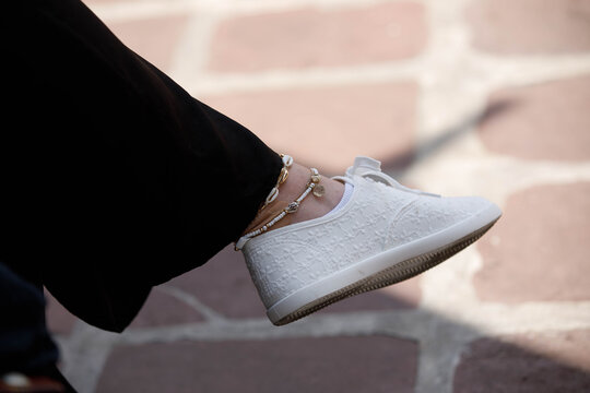 Female in white sneakers sitting cross-legged, in anklets, close up.