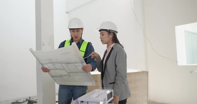 Male engineer and female architect review a building model, blueprints and a digital device at a residential construction site, planning design coordination and project development.
