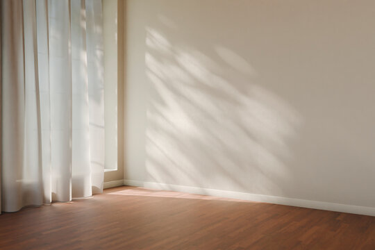 Minimalist empty room with sunlight and tree shadow. Modern cozy interior design background mockup with beige plaster wall, window curtain and wooden floor. Scandinavian living room scene.