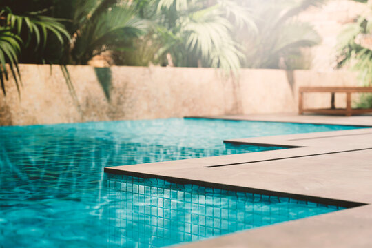 Luxury pool closeup edge with granite tiles and tropical garden. Summer travel hotel resort. Poolside product placement for beauty brand display. Modern aesthetic architecture design.