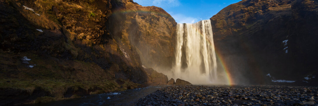 The Skagafoss waterfall, a tall cascade over a sheer cliff, mist and a Double Rainbow in the air.