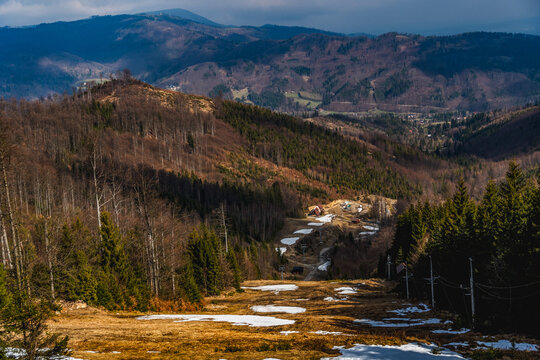 Spring mountain landscape with remaining snow patches on a ski slope surrounded by forested hills in the Beskid Mountains.