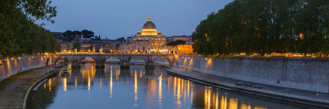 View of the Basilica of St Peter's at dusk across the Tiber River, panoramic view.