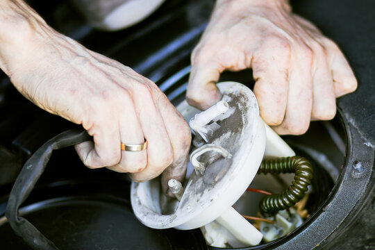 Close-up of hands of a technician repairing a car fuel pump assembly, showing intricate components and wiring inside a vehicle's fuel tank