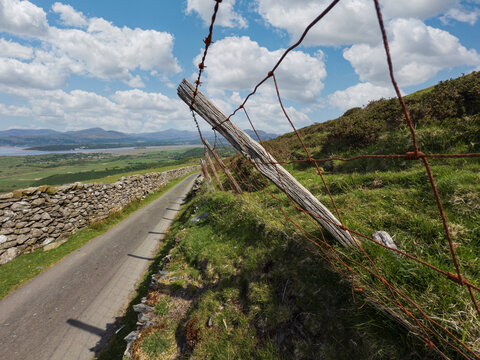A rural hard top road and a sheep fence of wood post and barbed wire with sheep wool attached.