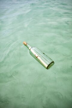 Glass bottle with a rolled note floats on clear Caribbean water. Concept of mystery, hope, or lost communication.