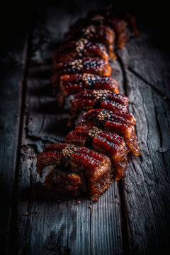 shot of a glazed Anago sea eel sushi at a 45 degree angle on a dark wooden surface. Muted natural color tones and hand-sliced uneven edges. Handcrafted rice with visible grains and handcrafted 