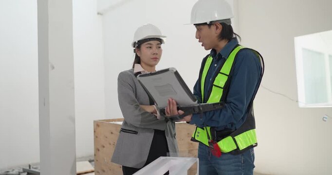 Male engineer and female architect review a building model, blueprints and a digital device at a residential construction site, planning design coordination and project development.
