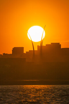 View of the Air Force Memorial spires silhouetted against a large setting sun over the city skyline and water in Washington, District of Columbia, United States.