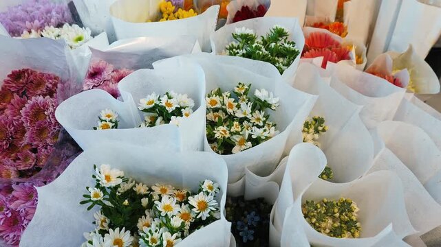 Mixed floral arrangements including Chrysanthemum and Bellis perennis in white paper wrap, flower market display, small business retail and floristry background, slow motion