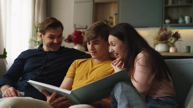 Cheerful adolescent son and his parents browsing a family photo album together