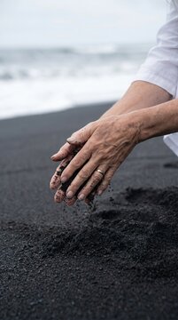 A close-up of a woman's hands sifting black volcanic sand