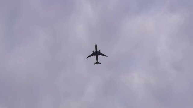 Camera panning with commercial airplane as it flies directly overhead through a moody, overcast grey sky during the daytime