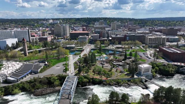 Spokane Washington downtown with river, bridges and riverside park, highlighting urban skyline, flowing water and scenic Pacific Northwest city landscape in United States. Aerial backwards wide shot.