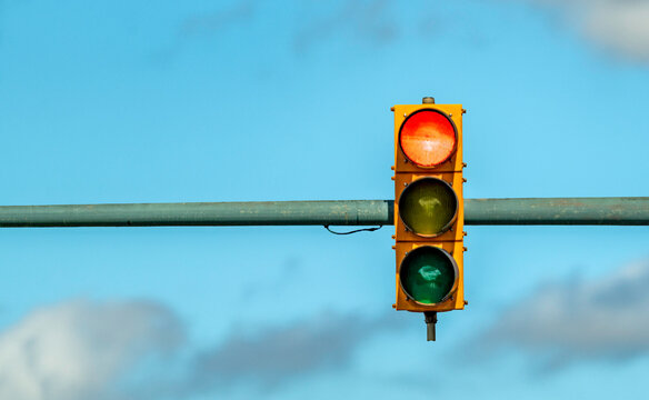 Red yellow and green stoplight traffic signal isolated against a blue sky with some clouds
