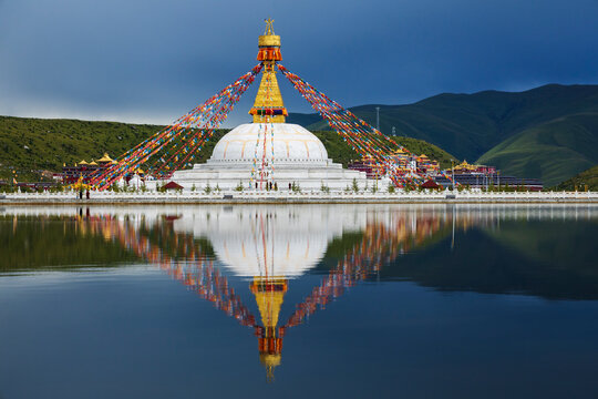 Stupa at the Zhuqing Wujian Zen Forest Monastery, decorated with prayer flags, reflections in the calm lake water.