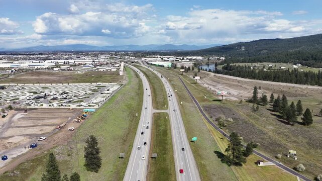 Stock Footage Description (189 Characters) Busy highway traffic on Interstate 90 flowing through scenic rolling hills and green landscape under sunny sky in Post Falls, Idaho, United States. Aerial