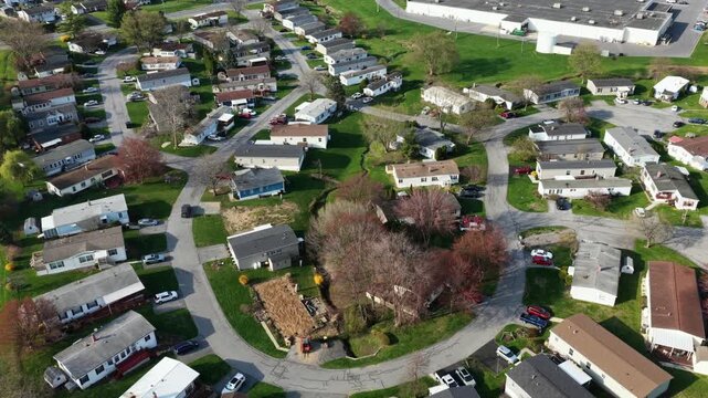 Curved suburban neighborhood with single level homes and mobile houses in Akron, PA surrounded by spring greenery, quiet streets and organized layout. Affordable residential living. Aerial flyover.