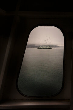 View through a ferry porthole window of the grey stormy weather in the San Juan Islands and the boat wake.