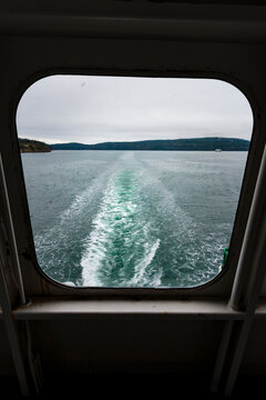 View through a ferry porthole window of the grey stormy weather in the San Juan Islands and the boat wake.