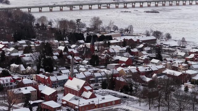 Snow covered city of Wrightsville, PA with colorful row houses church steeples and frozen river in background during winter season showing small town landscape and architecture. Aerial tilt up wide.
