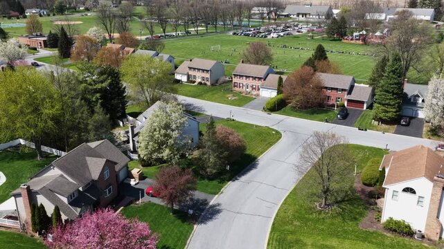 Aerial drone flyover of calm suburban neighborhood in United States during spring, with single-family homes, curved residential streets, green lawns and blooming trees in peaceful setting