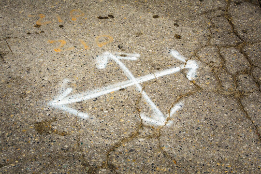 Multl-direction chalk arrows on pavement, cracks in the surface, potholes and concrete for repair.