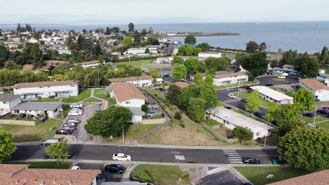 Multi family apartment community in Rodeo California near waterfront with rows of residential buildings, streets and green spaces in quiet suburban neighborhood in USA. Aerial approaching shot.