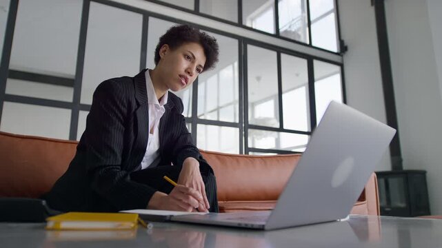 Businesswoman taking notes during video call on laptop