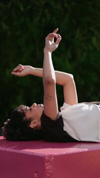 young woman engages in expressive dance improvisation outdoors, reclining on vibrant pink block. fluidity and spontaneity of her movements. sense of freedom and creativity in dance. slow motion
