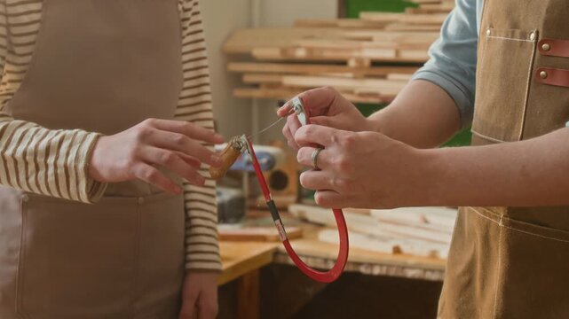 Midsection shot of anonymous woodworker showing coping saw to unknown child touching its blade during masterclass, both wearing aprons