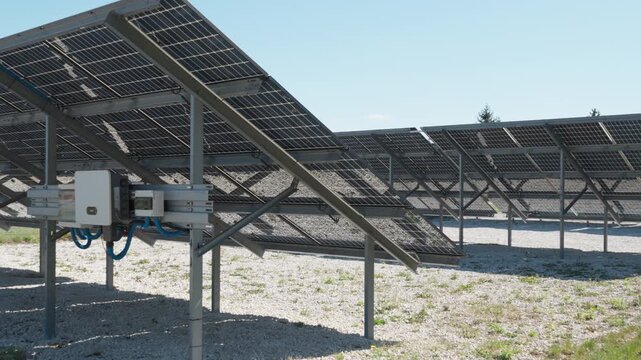 Bifacial photovoltaic solar panels and inverter mounted on metal racking. Industrial renewable energy farm using white gravel for albedo effect to optimize power generation yield.