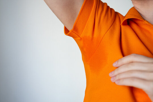 Anonymous woman showing perspiration stain under arm indoors. Concept of excessive sweating, deodorant protection, personal hygiene and summer discomfort. 