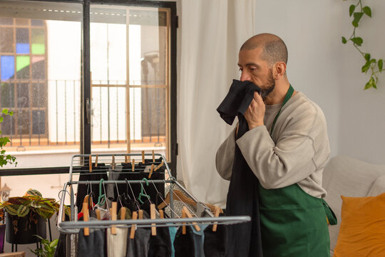 Hispanic man checking dryness of clothes by smelling garment at home