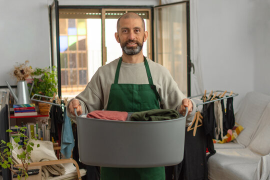 Bearded Hispanic man smiling with basket of clean folded clothes