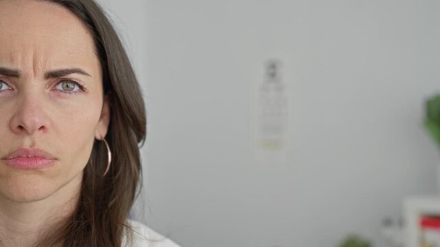 Woman doctor frowning with furrowed brow, face and snellen eye chart visible in medical building, hoop earring visible; concerned reflection.