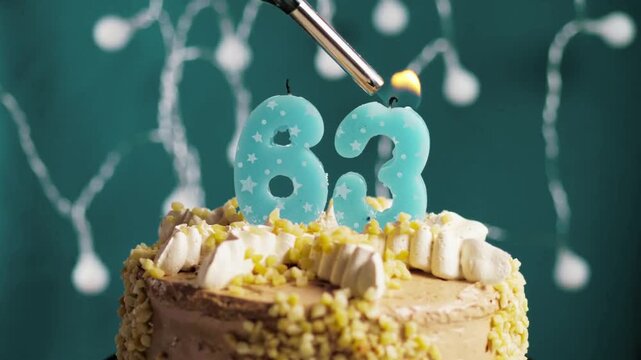 Birthday cake with a glowing number 63 candle placed on a blue background captures a beautiful milestone celebration in slow motion and close-up view.