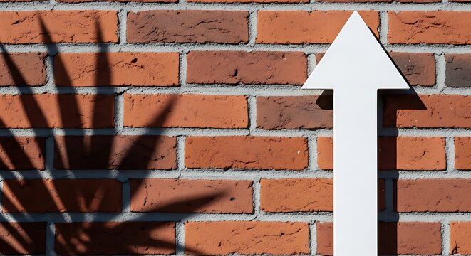 White arrow sign pointing upward on red brick wall with shadow
