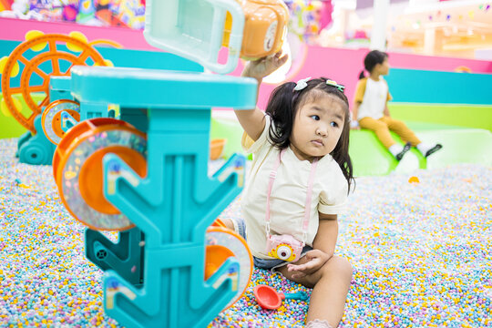 Cute little Asian girl playing in a colorful ball pit at an indoor playground,A lovely young Asian girl with pigtails enjoying her time sitting among thousands of colorful small plastic balls.