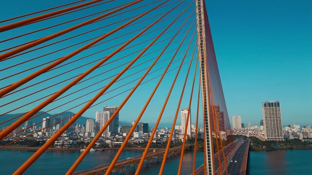 aerial drone view of suspension cable bridge over Han river in Danang, geometric cable-stayed bridge architecture with modern city skyline and roadway, Da Nang Vietnam 4k