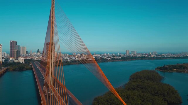 aerial drone view of suspension cable bridge over Han river in Danang, geometric cable-stayed bridge architecture with modern city skyline and roadway, Da Nang Vietnam 4k