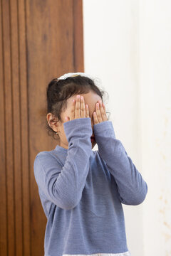 A daugther playing hide and seek, covering her face with both hands
