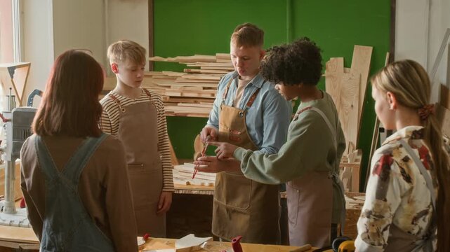 Zoom in shot of two multiethnic teenage boys testing sharpness of coping saw while young carpenter giving instructions to group on how to use this woodworking tool